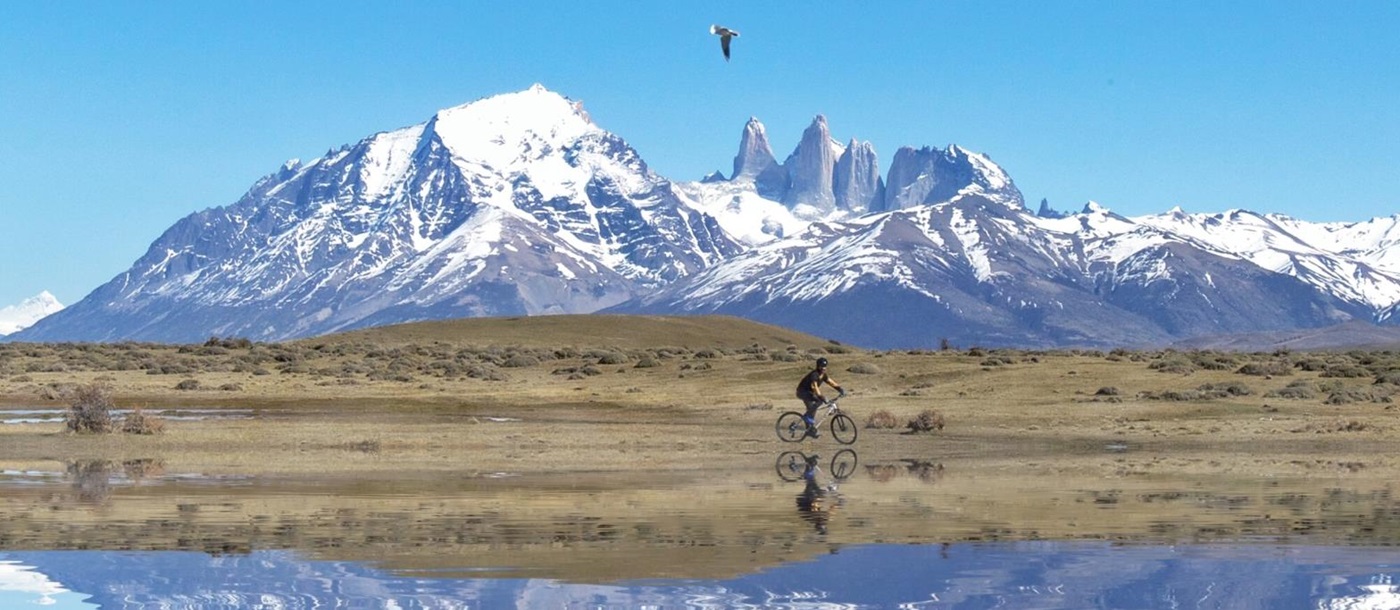 Mirror-like reflection of a cyclist withsnowy mountains in the background