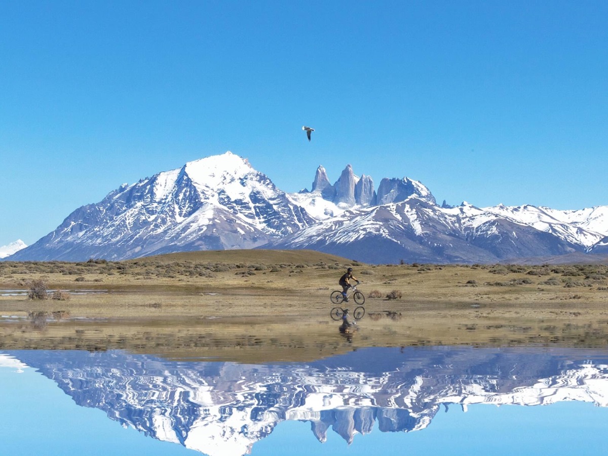 Mirror-like reflection of a cyclist withsnowy mountains in the background