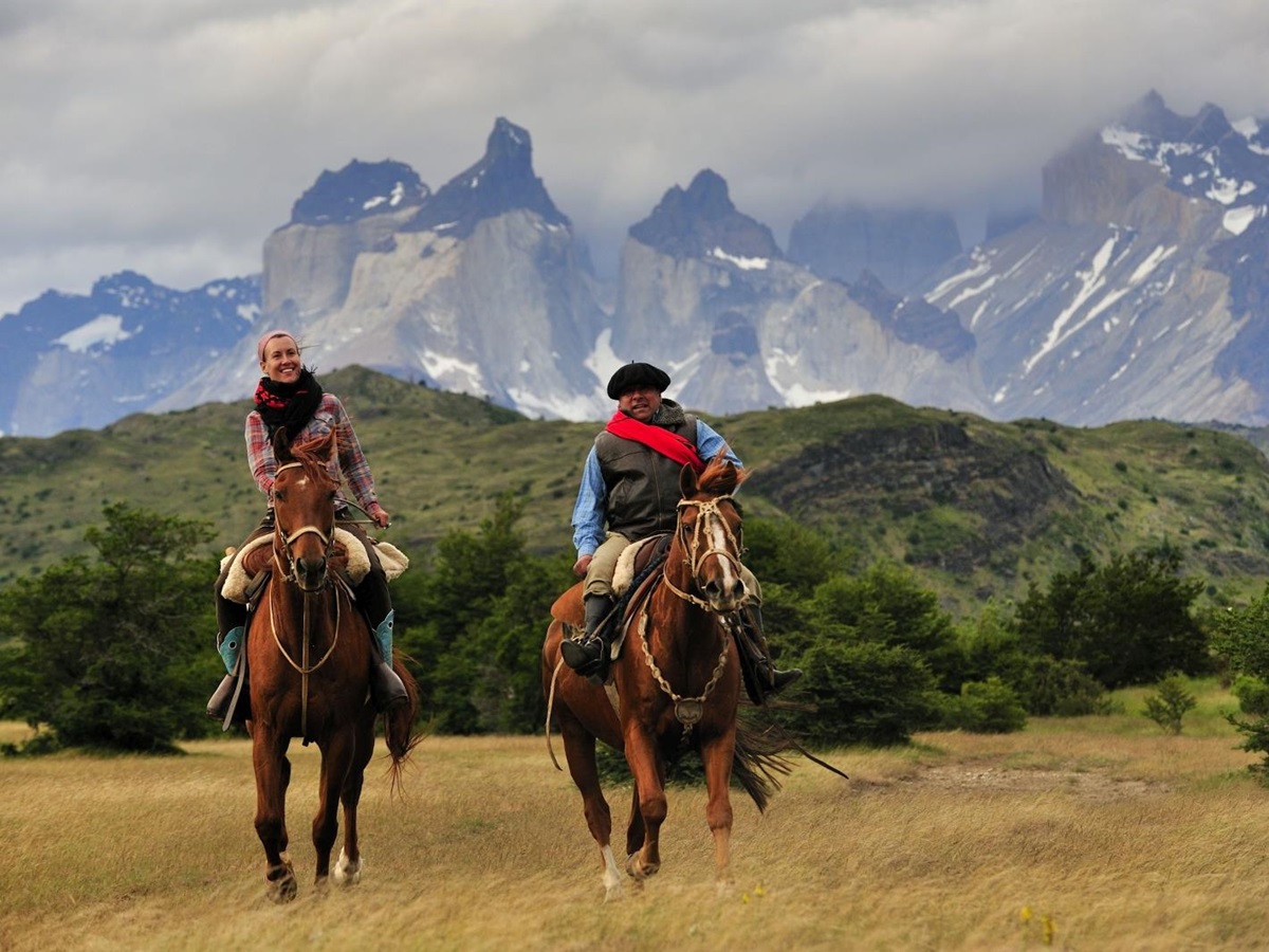 Two people riding horses with mountain range backdrop