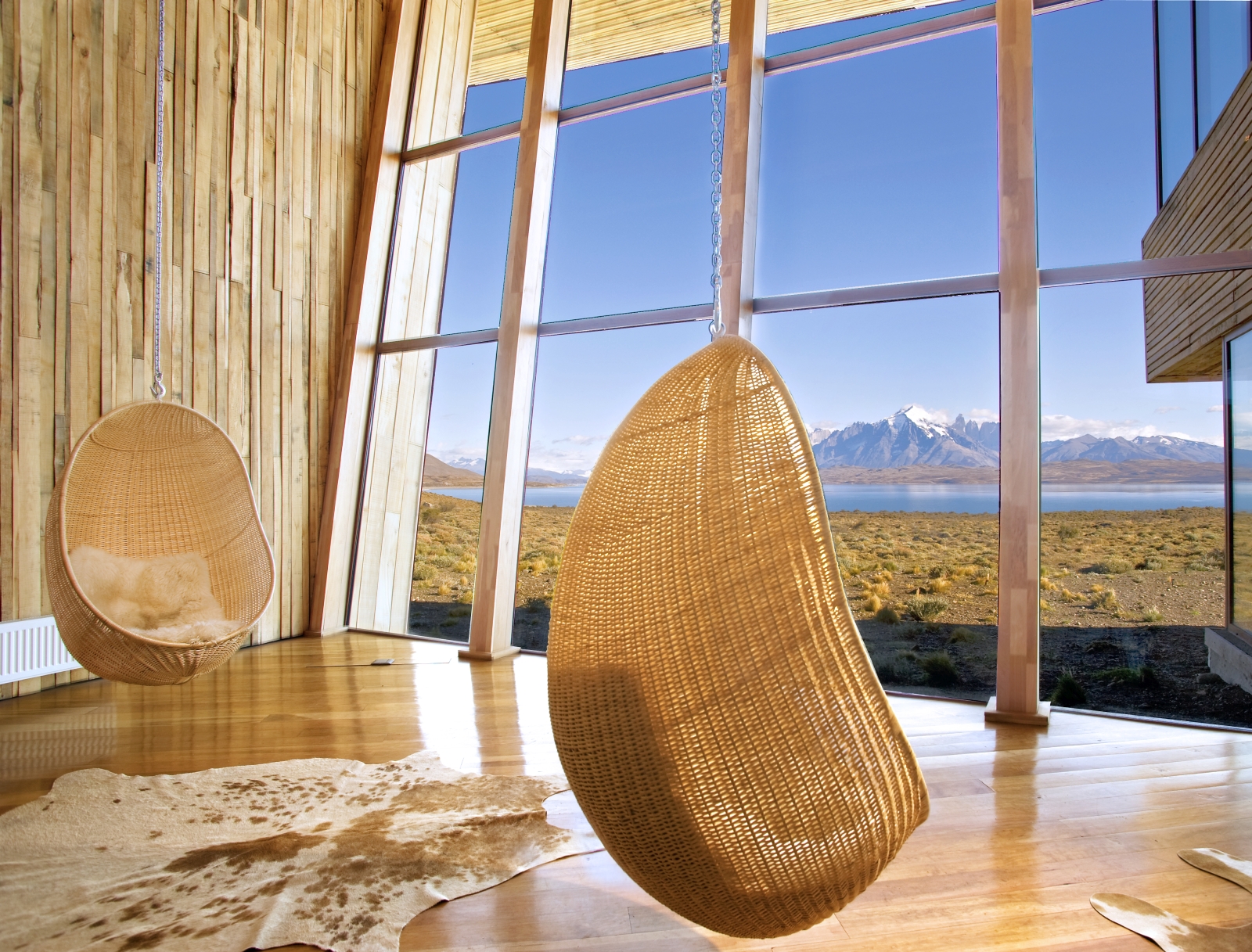 Two hanging chair egg chairs in front of a glasss wall overlooking the scenery at Tierra Patagonia
