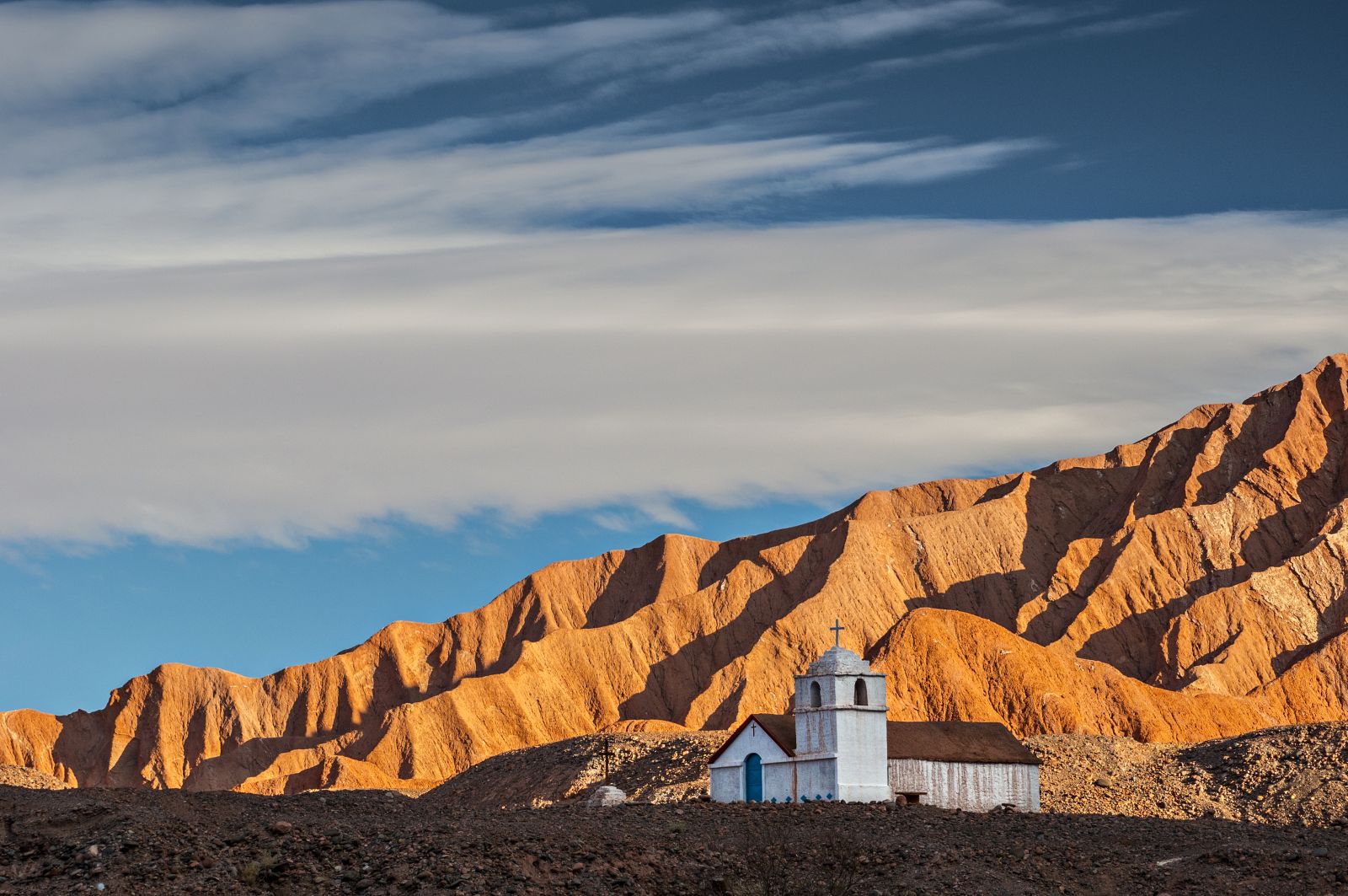 Small white chapel against the backdrop of red mountains in the Atacama Desert, Chile