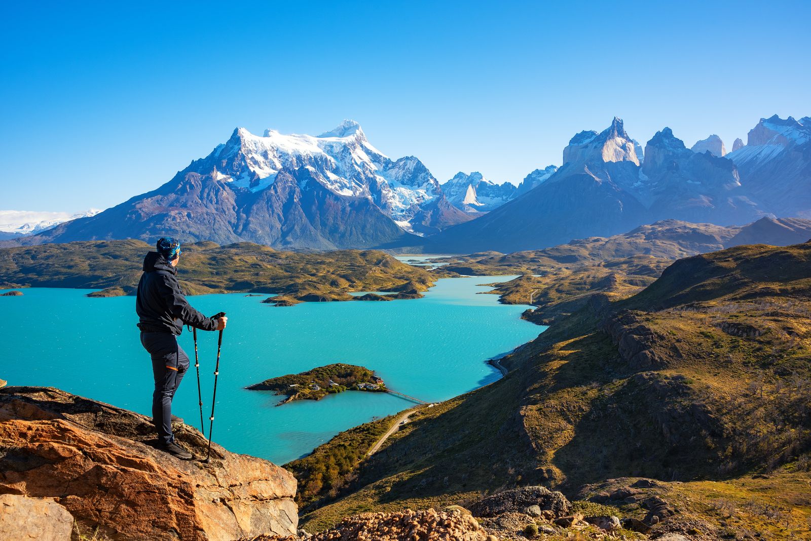 A hiker looking out over a dazzling turquoise lake and the Torres del Paine horns in Patagonia Chile