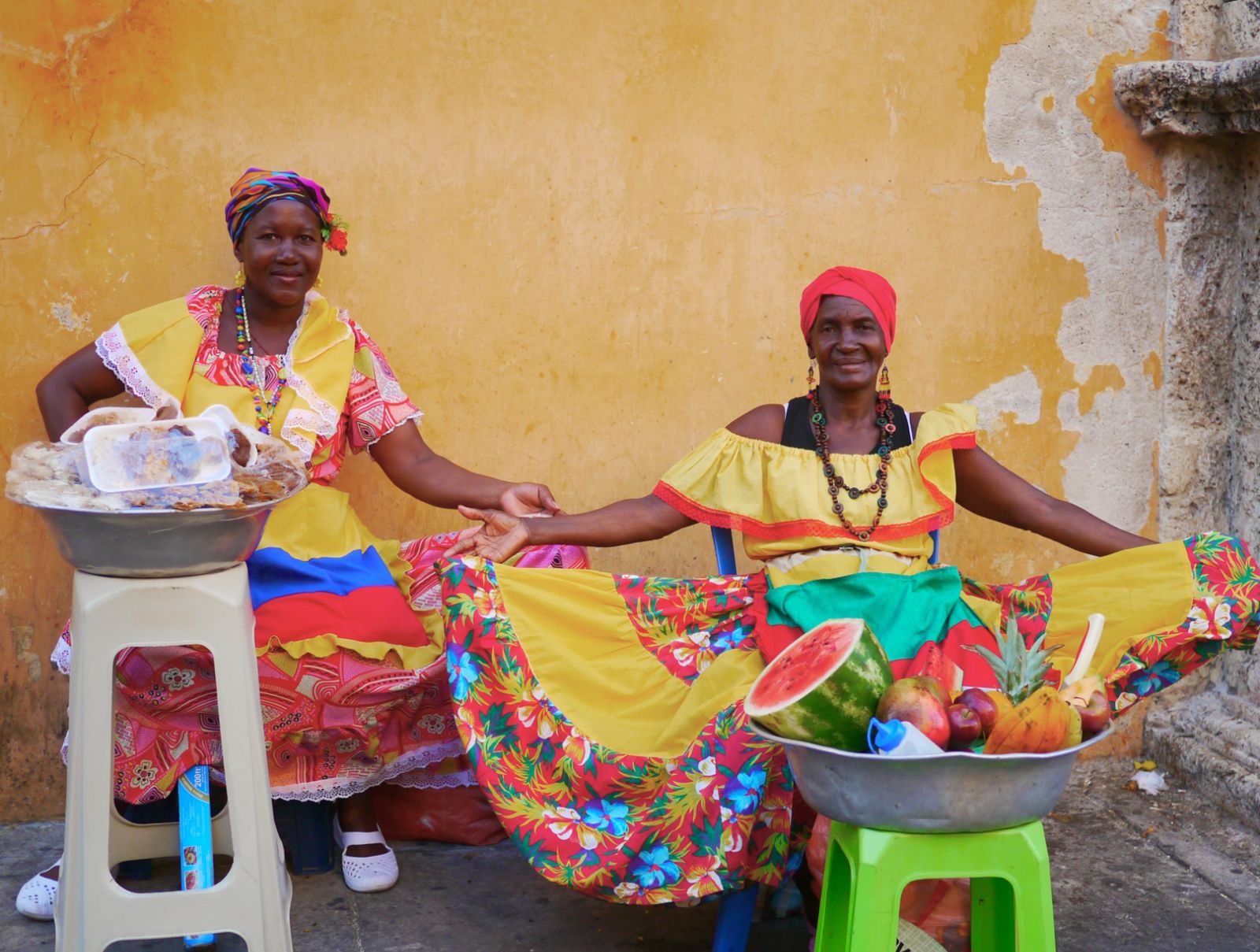 Two local ladies in colourful dresses selling fruit in a street in Cartagena, Colombia