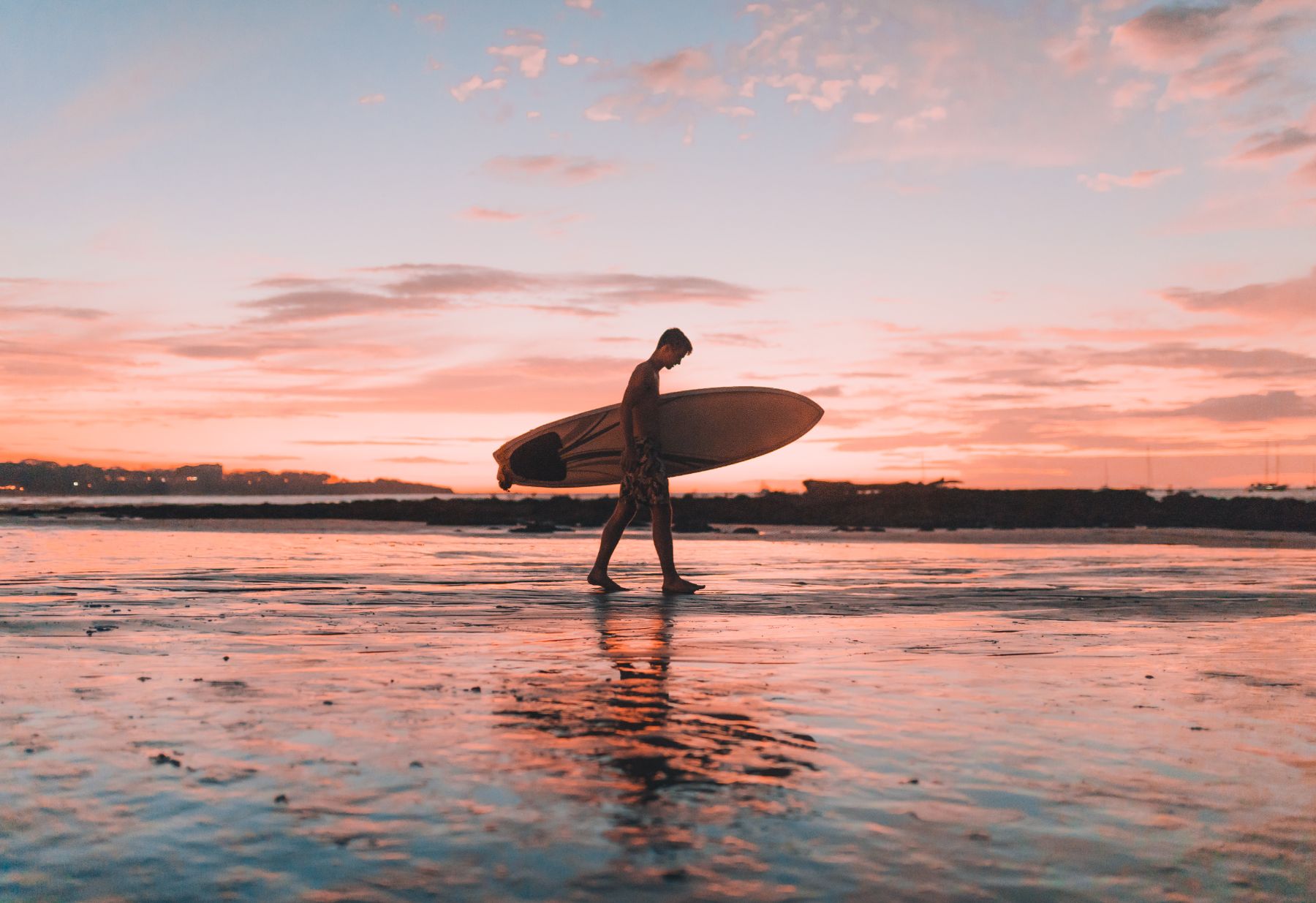 Man walking along a Costa Rican beach with a surf board at sunset