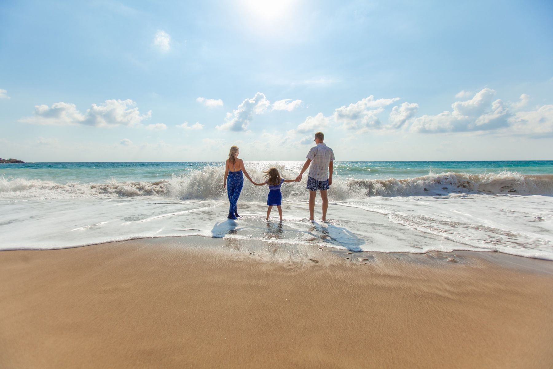 Parents and a young child paddling on a golden sand beach