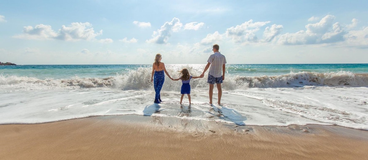 Parents and a young child paddling on a golden sand beach