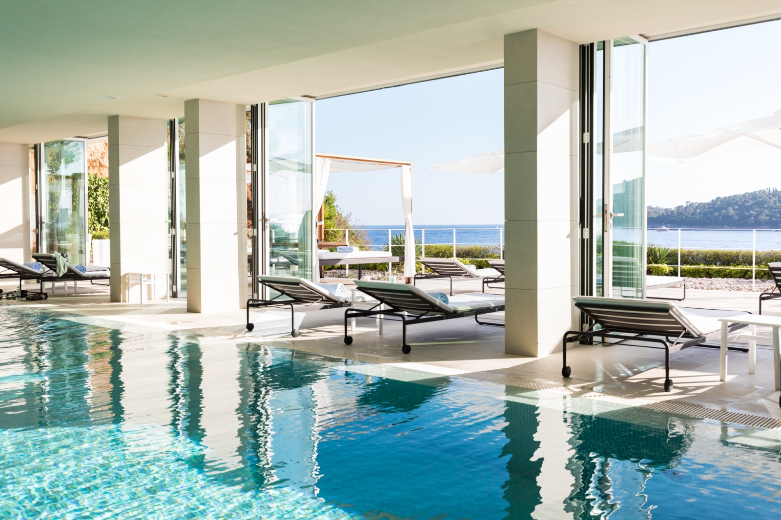 Indoor swimming pool with sun loungers and floor-to-ceiling windows overlooking the Mediterranean Sea at luxury hotel Villa Dubrovnik in Croatia