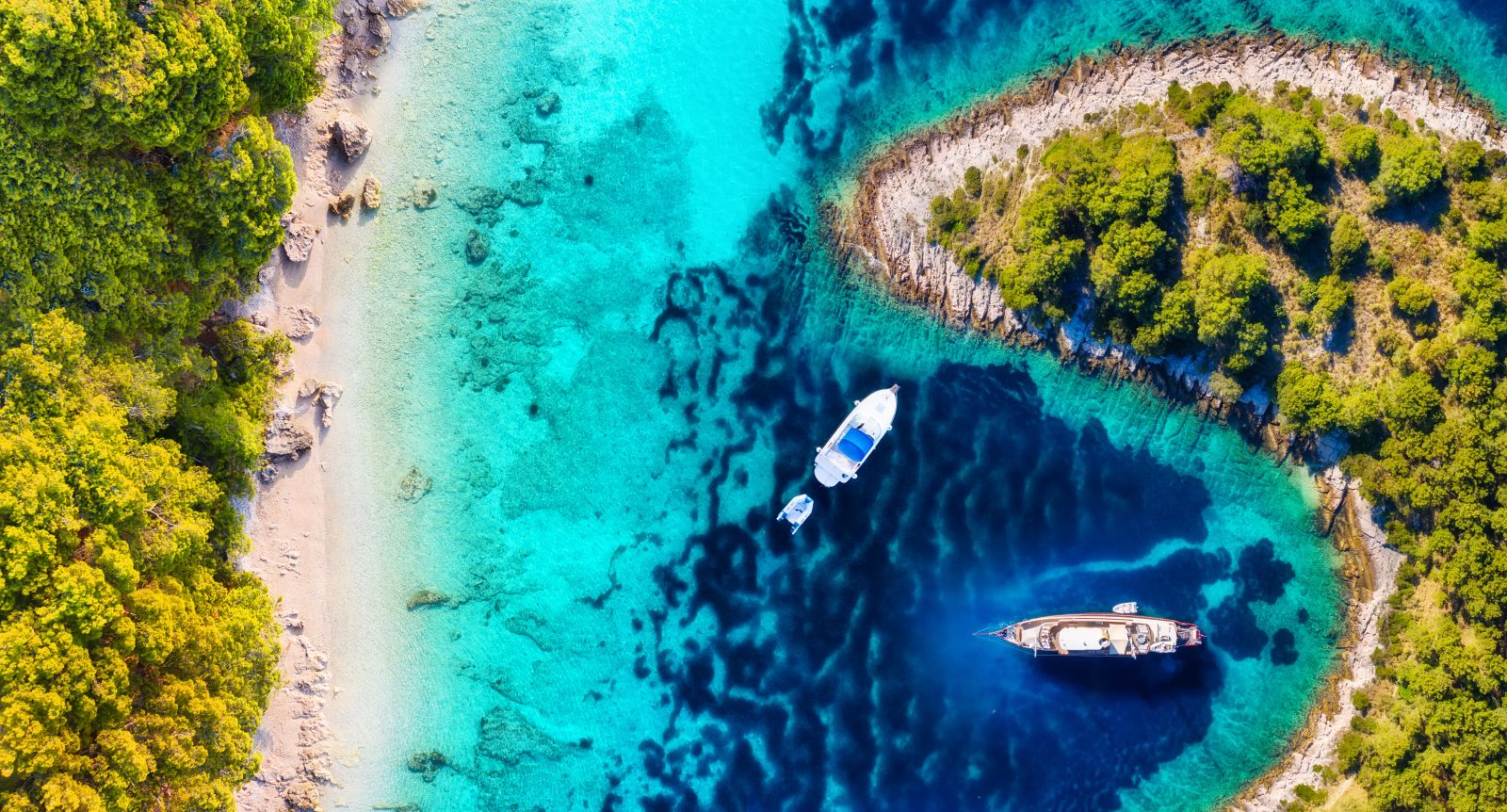 Aerial view of yachts moored off white sand beaches backed by forest in Croatia