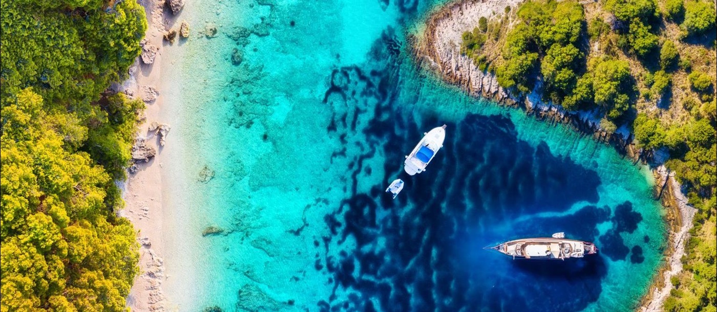 Aerial view of yachts moored off white sand beaches backed by forest in Croatia