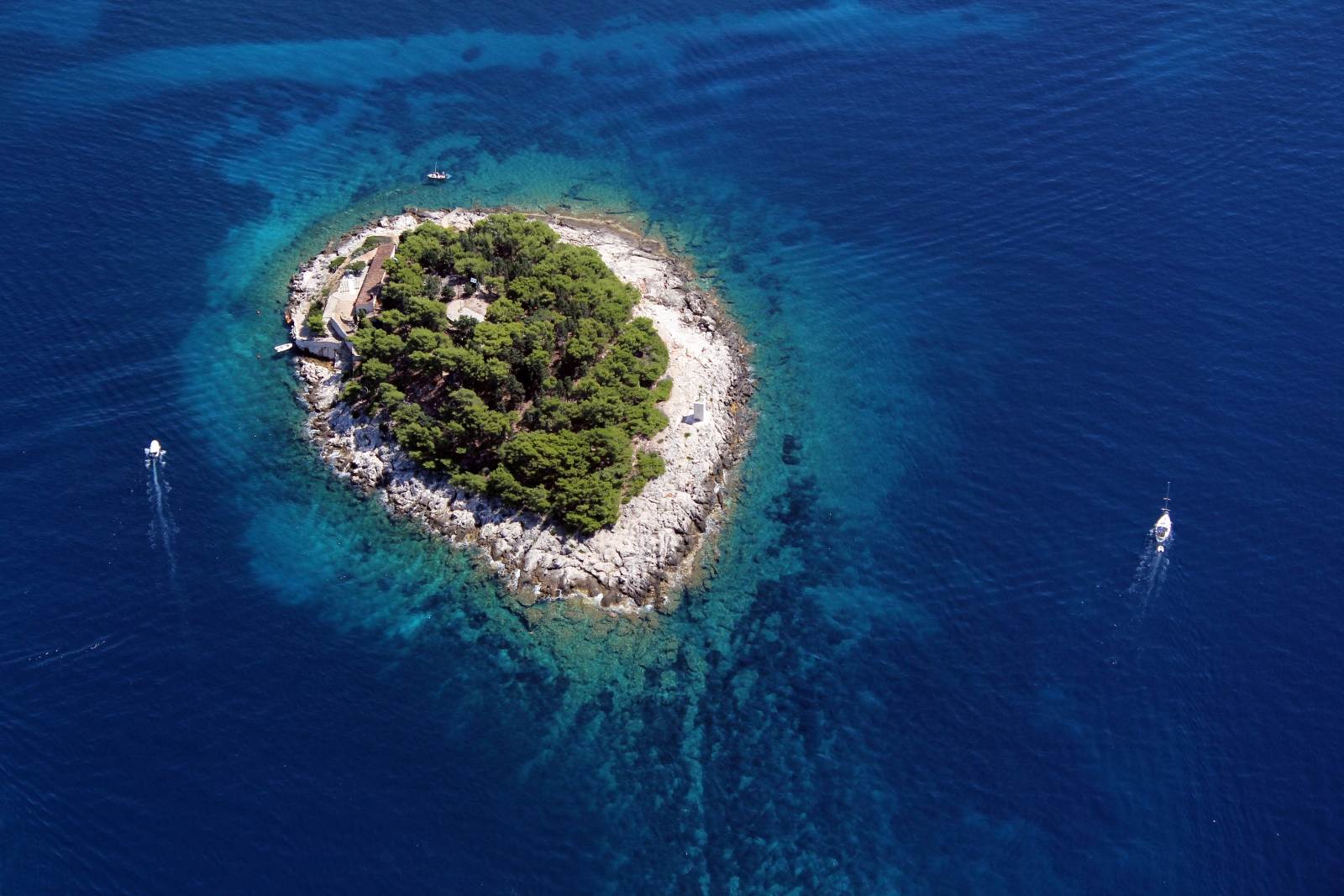 Aerial of single island with two speedboats circling