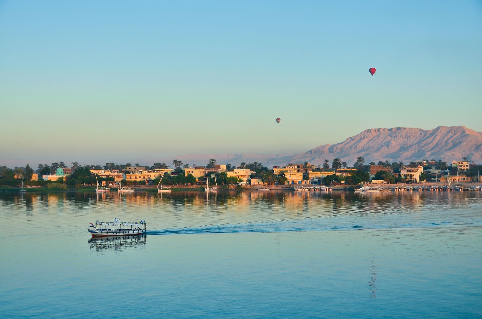 A small cruise ship on the River Nile with the Valley of the Kings in the background