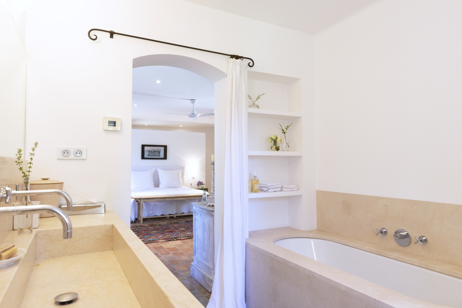 Ensuite bathroom with double sinks, mirror, bath, shelves, curtain and flowers at La Cadiere on the Cote d’Azur, France