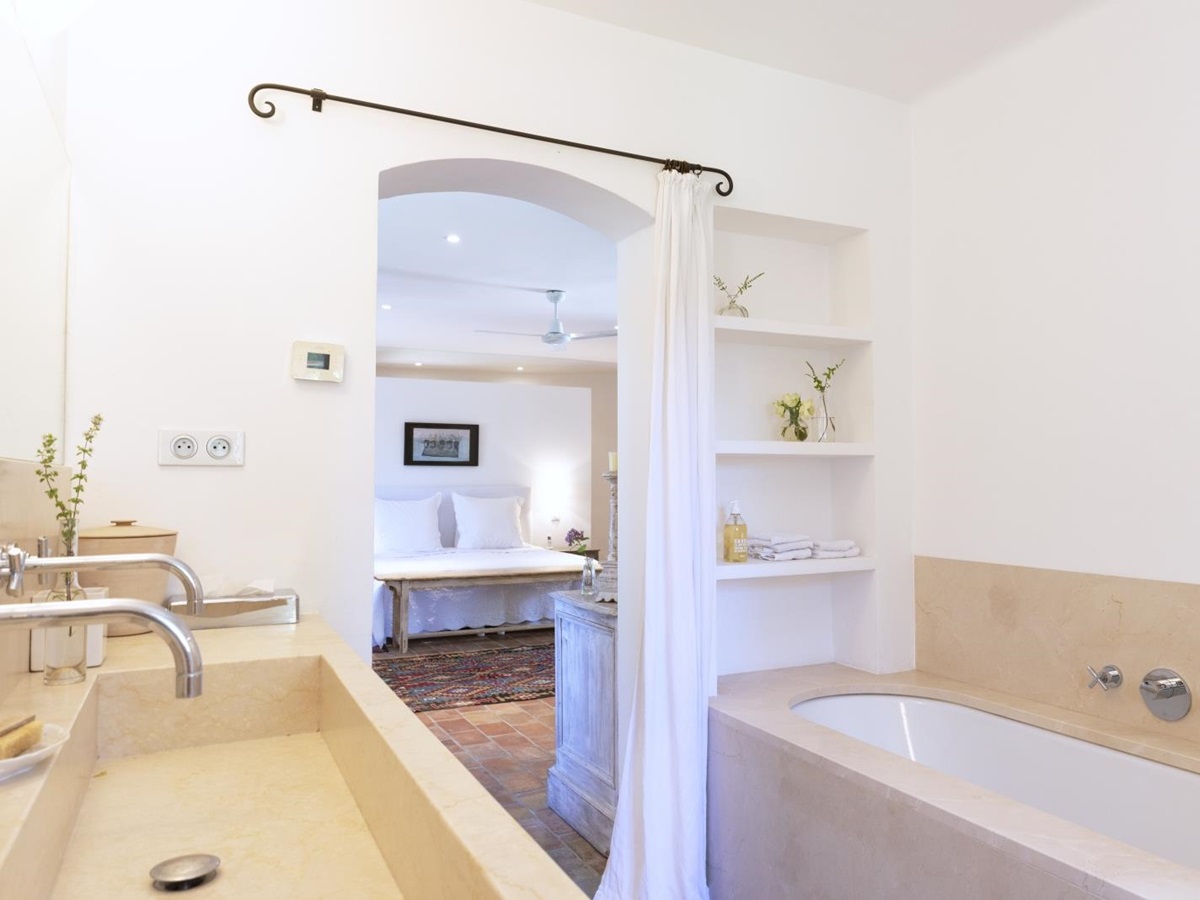 Ensuite bathroom with double sinks, mirror, bath, shelves, curtain and flowers at La Cadiere on the Cote d’Azur, France