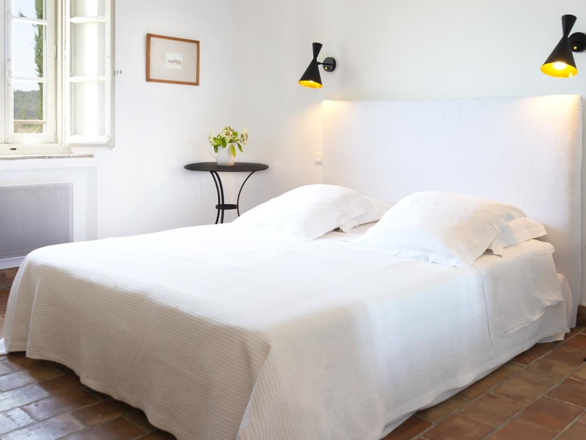 Bedroom with double bed, lamps, chair, table, flowers and picture frame at La Cadiere on the Cote d’Azur, France