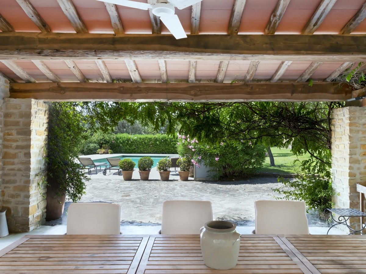 Covered outdoor dining area with table, chairs, vase, ceiling fan and pool view at La Cadiere on the Cote d’Azur, France