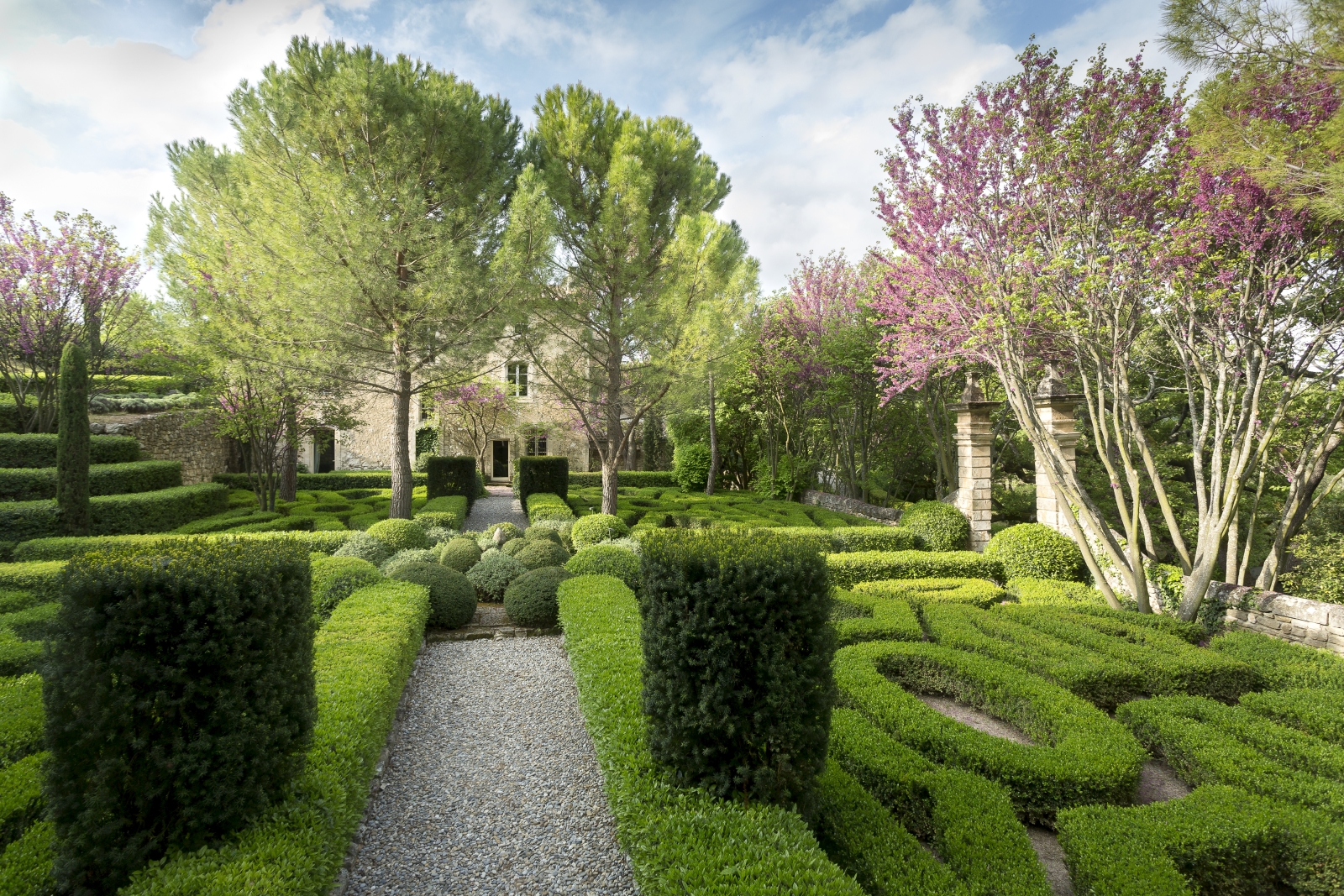 Façade of villa and gardens with trees, blossom, hedges and maze at Bastide Luberon in Provence, France