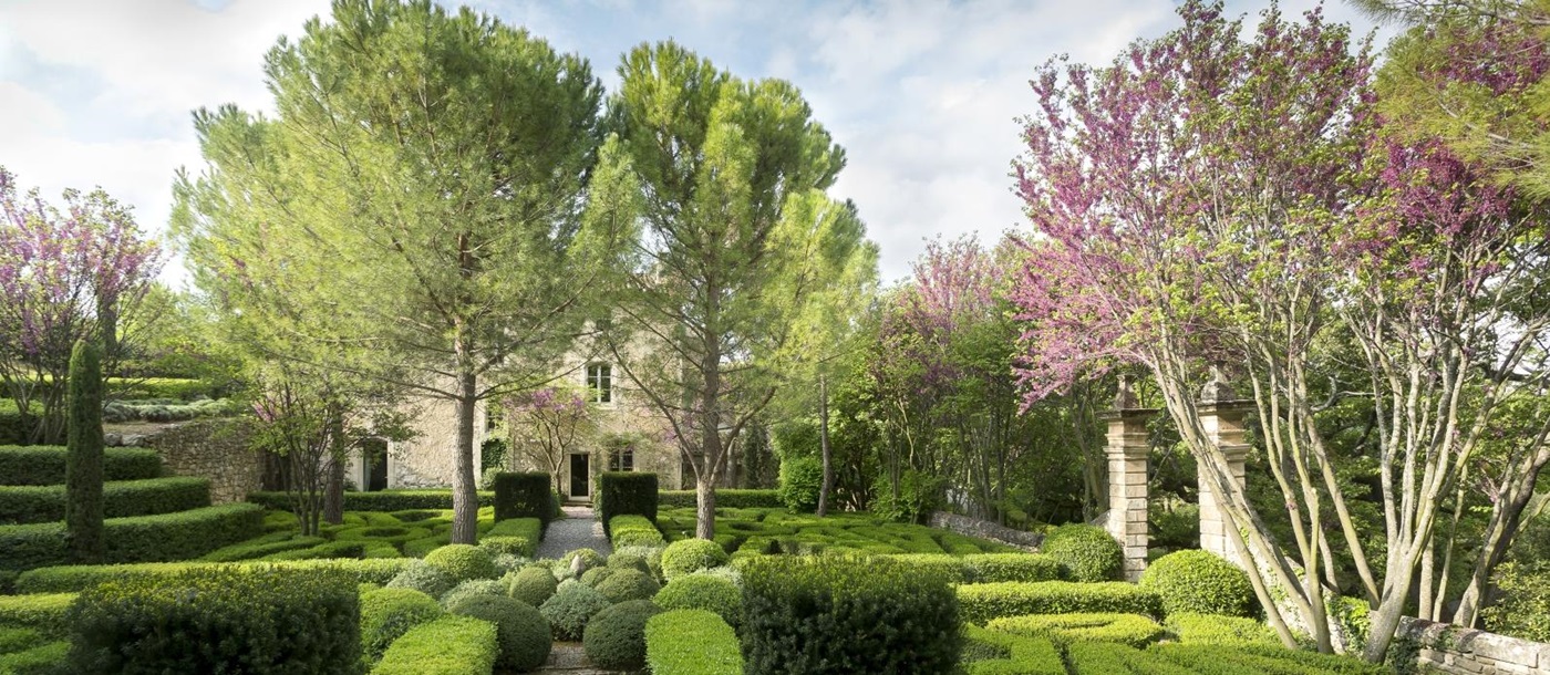 Façade of villa and gardens with trees, blossom, hedges and maze at Bastide Luberon in Provence, France