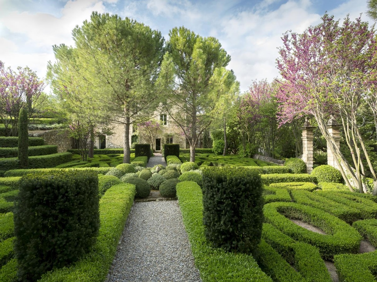 Façade of villa and gardens with trees, blossom, hedges and maze at Bastide Luberon in Provence, France