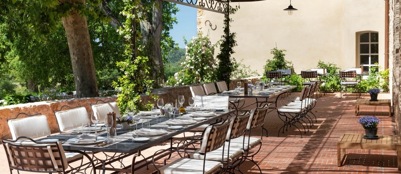 Covered outdoor dining area with long tables, chairs, place settings and flowers at Chateau Margui in Provence, France