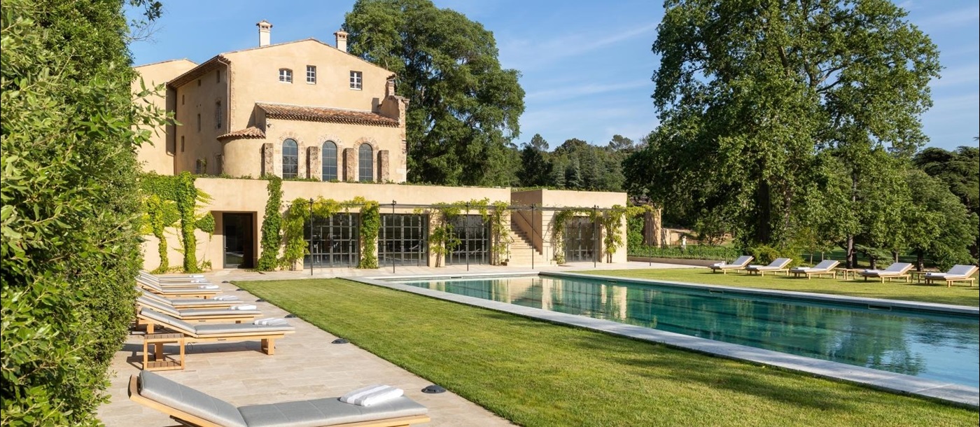 Pool and pool area with lawn, sun loungers, trees and view of villa at Chateau Margui in Provence, France