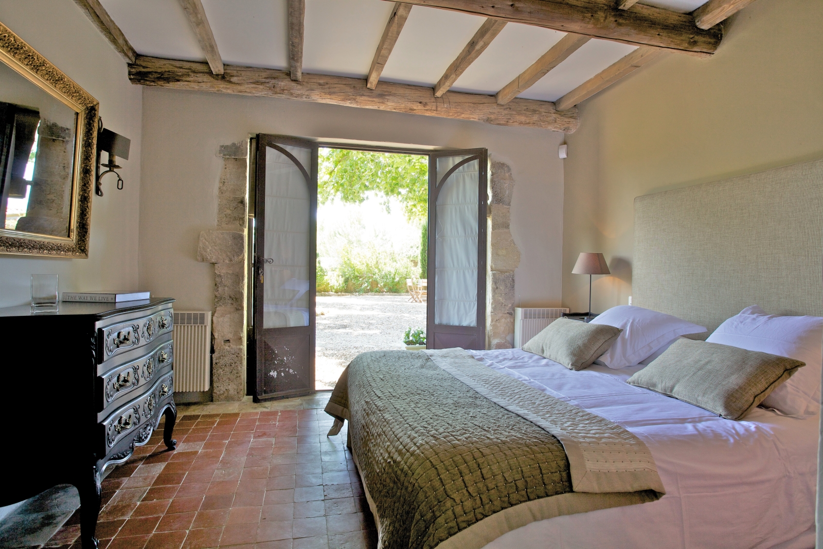 Bedroom with double bed, bedside table, lamp, drawers, mirror & French doors to terrace at Le Pont Romain in Provence, France