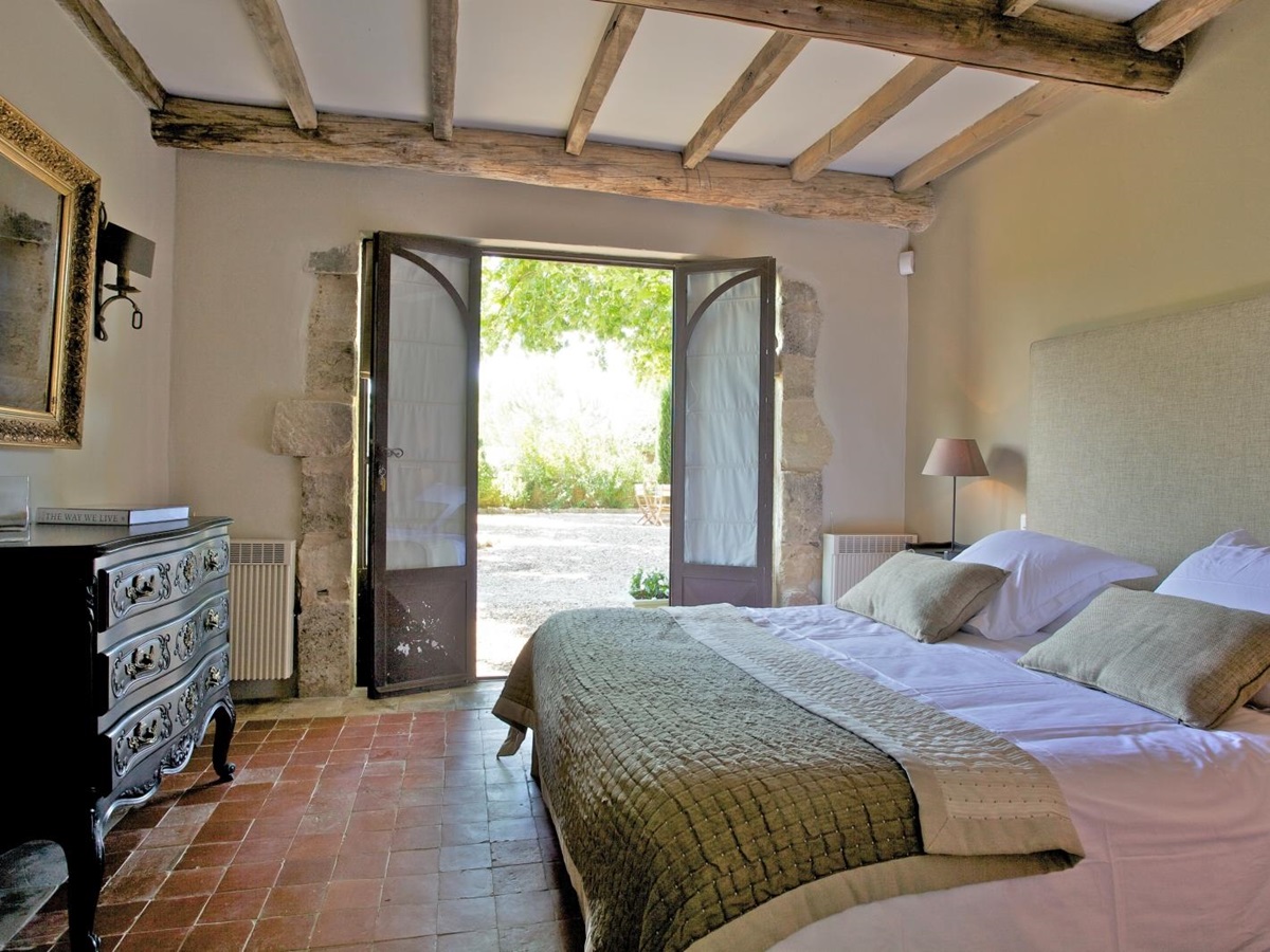 Bedroom with double bed, bedside table, lamp, drawers, mirror & French doors to terrace at Le Pont Romain in Provence, France