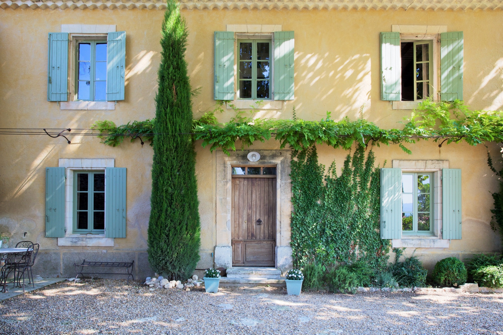 Main façade with vines, flowers, tree and shutters at Le Pont Romain in Provence, France