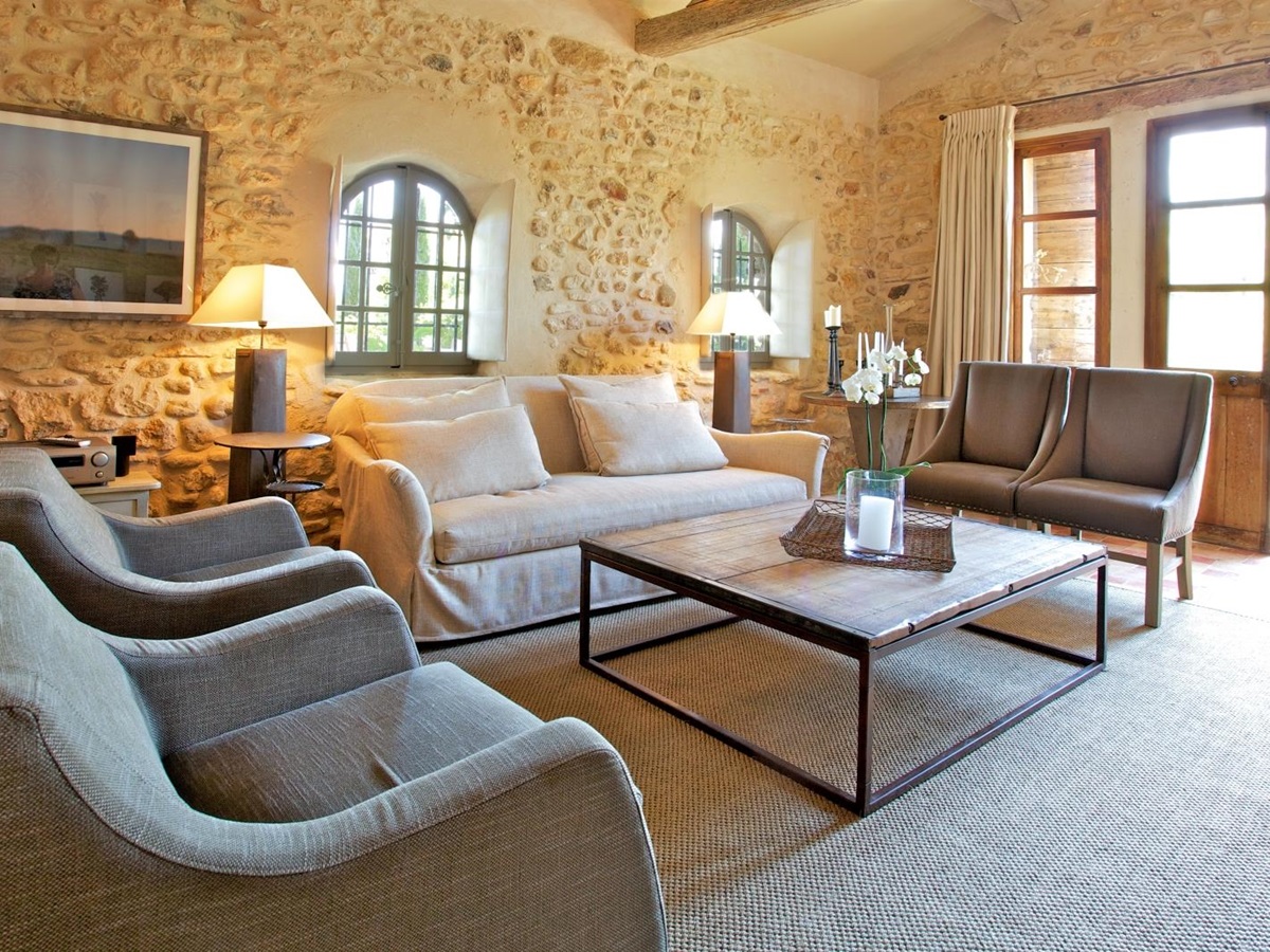 Living room with armchairs, sofa, tables, lamps and French doors to patio at Le Pont Romain in Provence, France