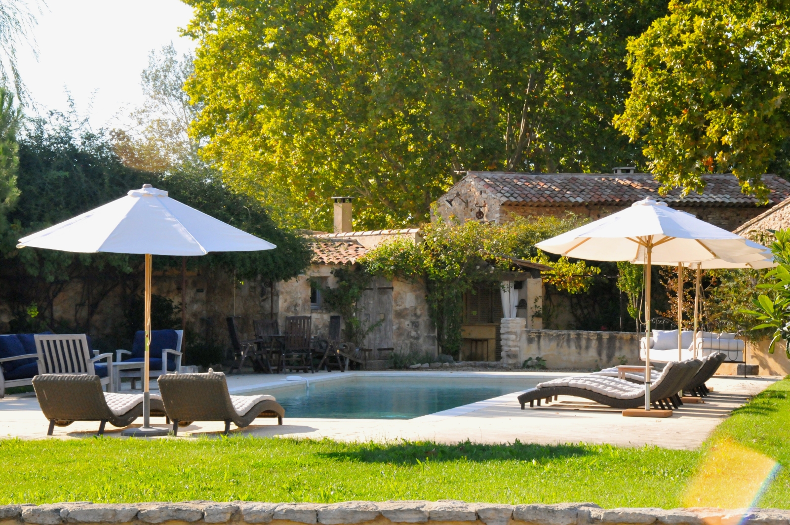 Pool and pool area with sun loungers, umbrellas, dining table and green grass at Le Pont Romain in Provence, France