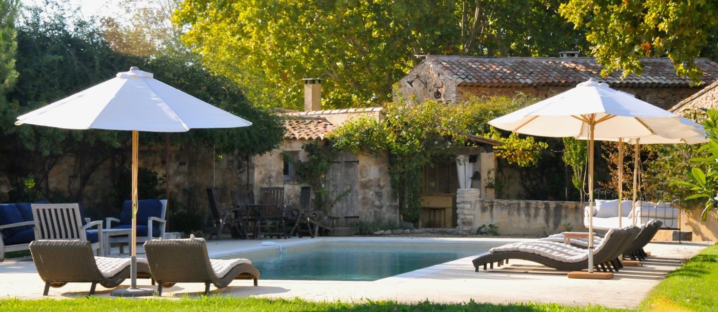 Pool and pool area with sun loungers, umbrellas, dining table and green grass at Le Pont Romain in Provence, France