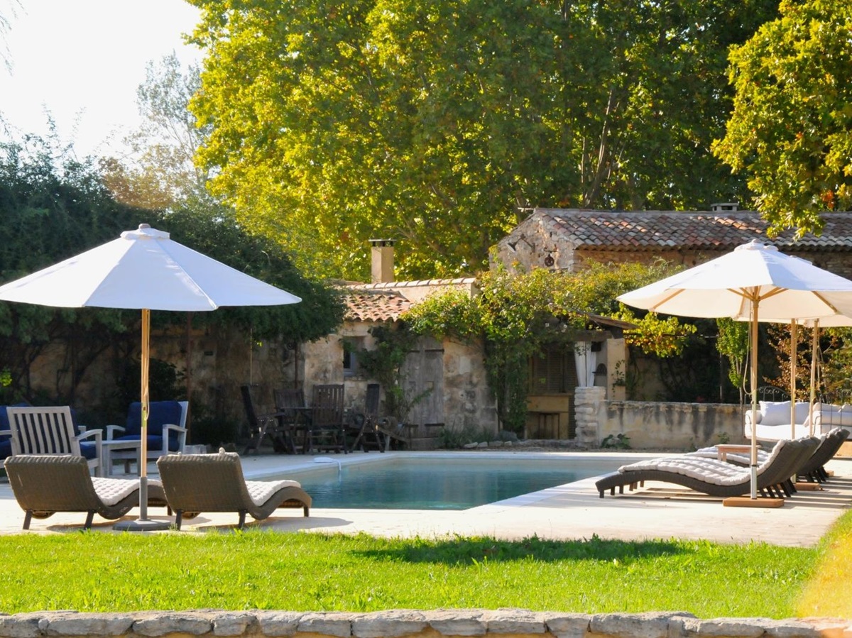 Pool and pool area with sun loungers, umbrellas, dining table and green grass at Le Pont Romain in Provence, France