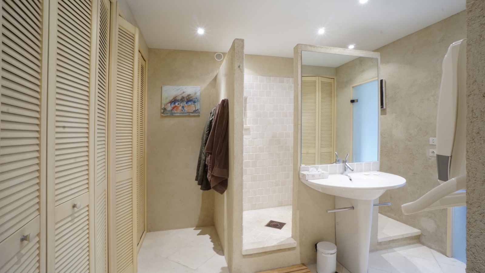 Bathroom with cupboards, sink, mirror, painting and large shower at Les Rochers in Provence, France