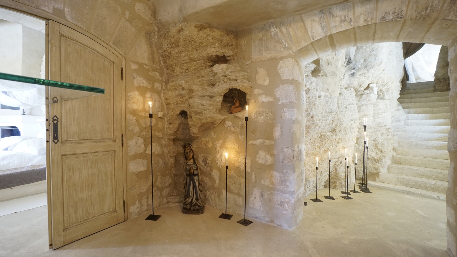 Hallway with stone walls, statues, candles and stone staircase at Les Rochers in Provence, France
