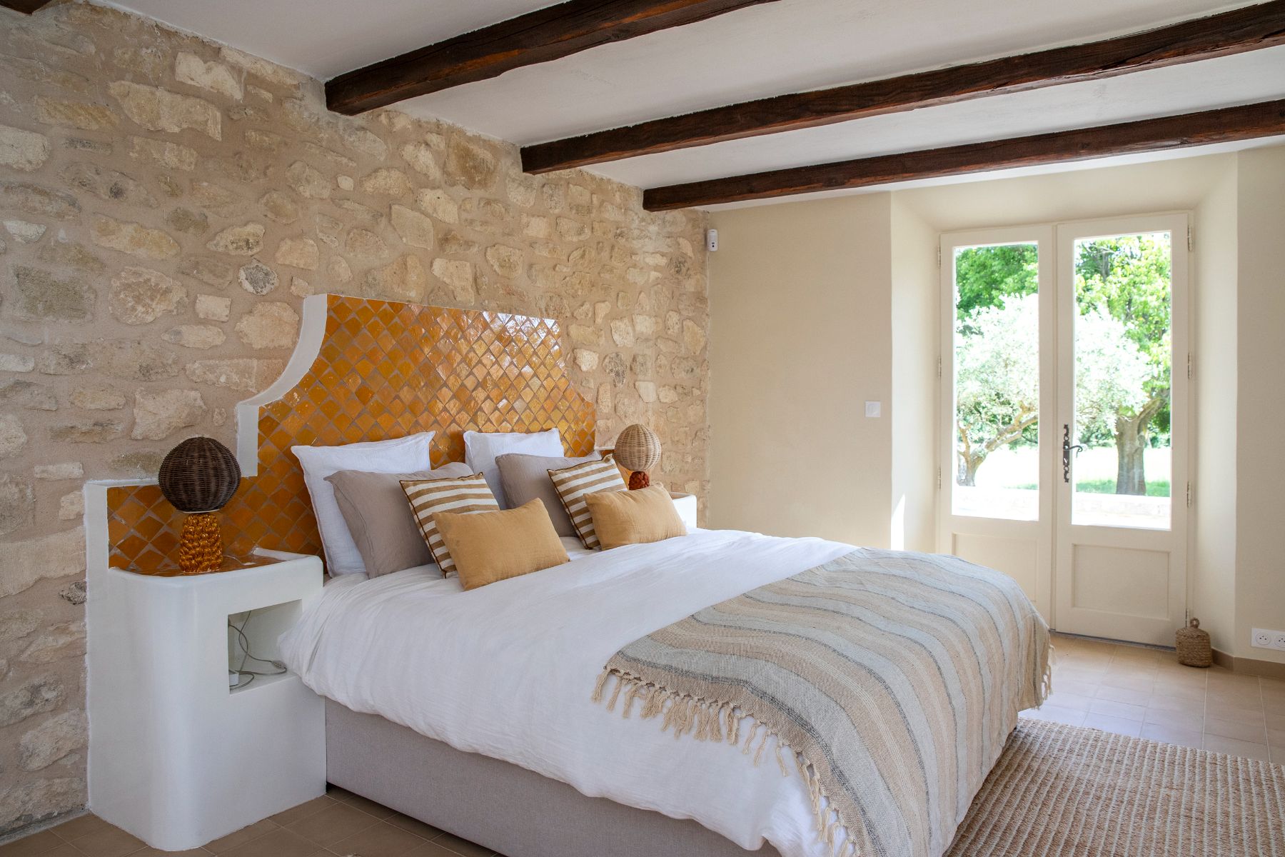 Bedroom with natural stone wall, oak beamed ceiling and double bed at Maison Les Baux in Provence, France