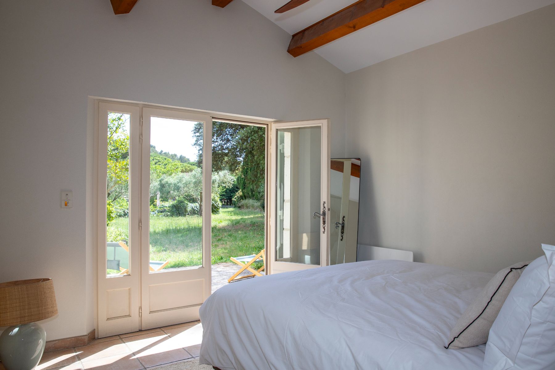 Bedroom in neutral white, with French windows opening onto the garden at luxury villa Maison Les Baux in Provence, France