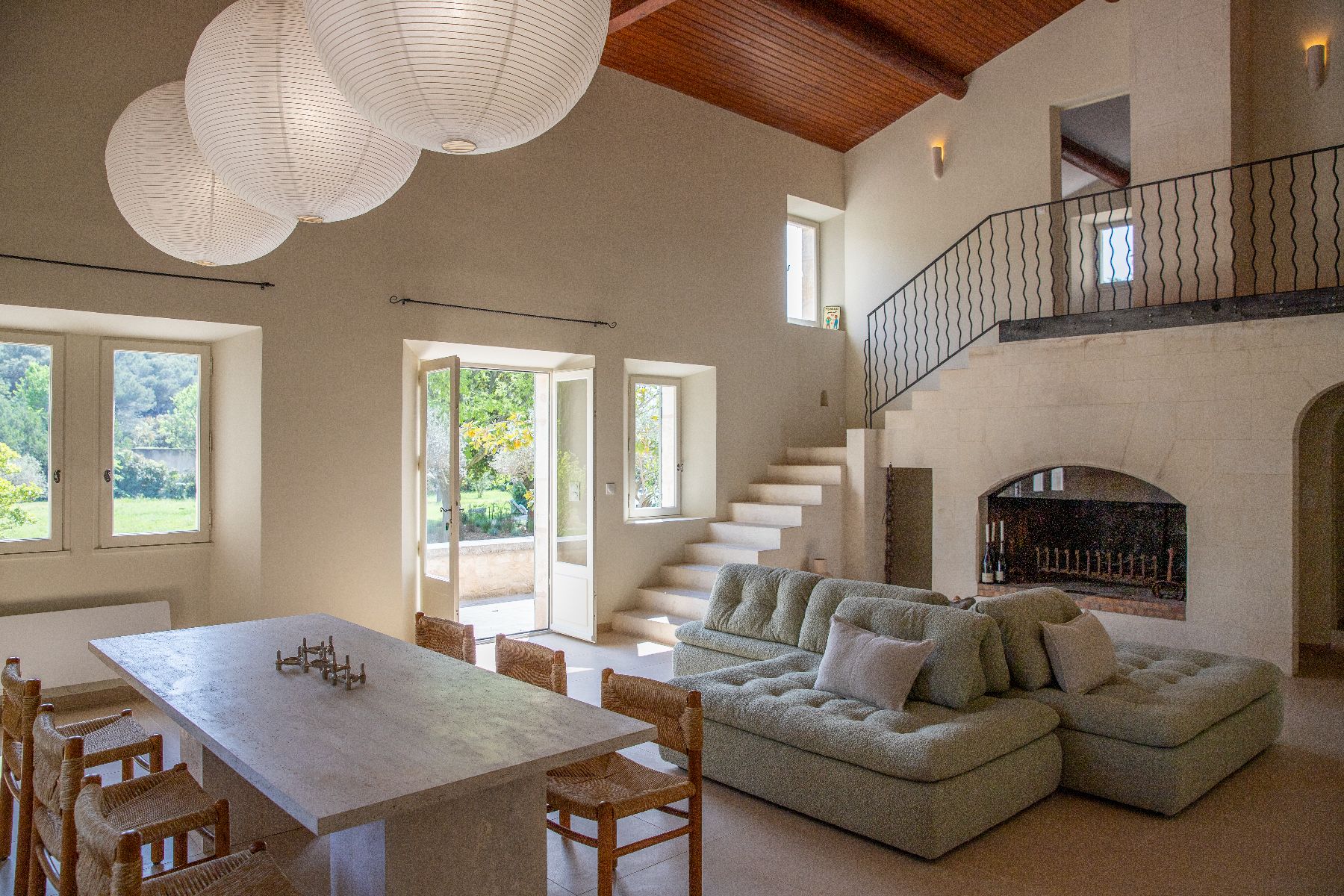 Living area with dining table in the foreground, and sofas opposite a fireplace, with stairs to upper level at Maison Les Baux in Provence, France
