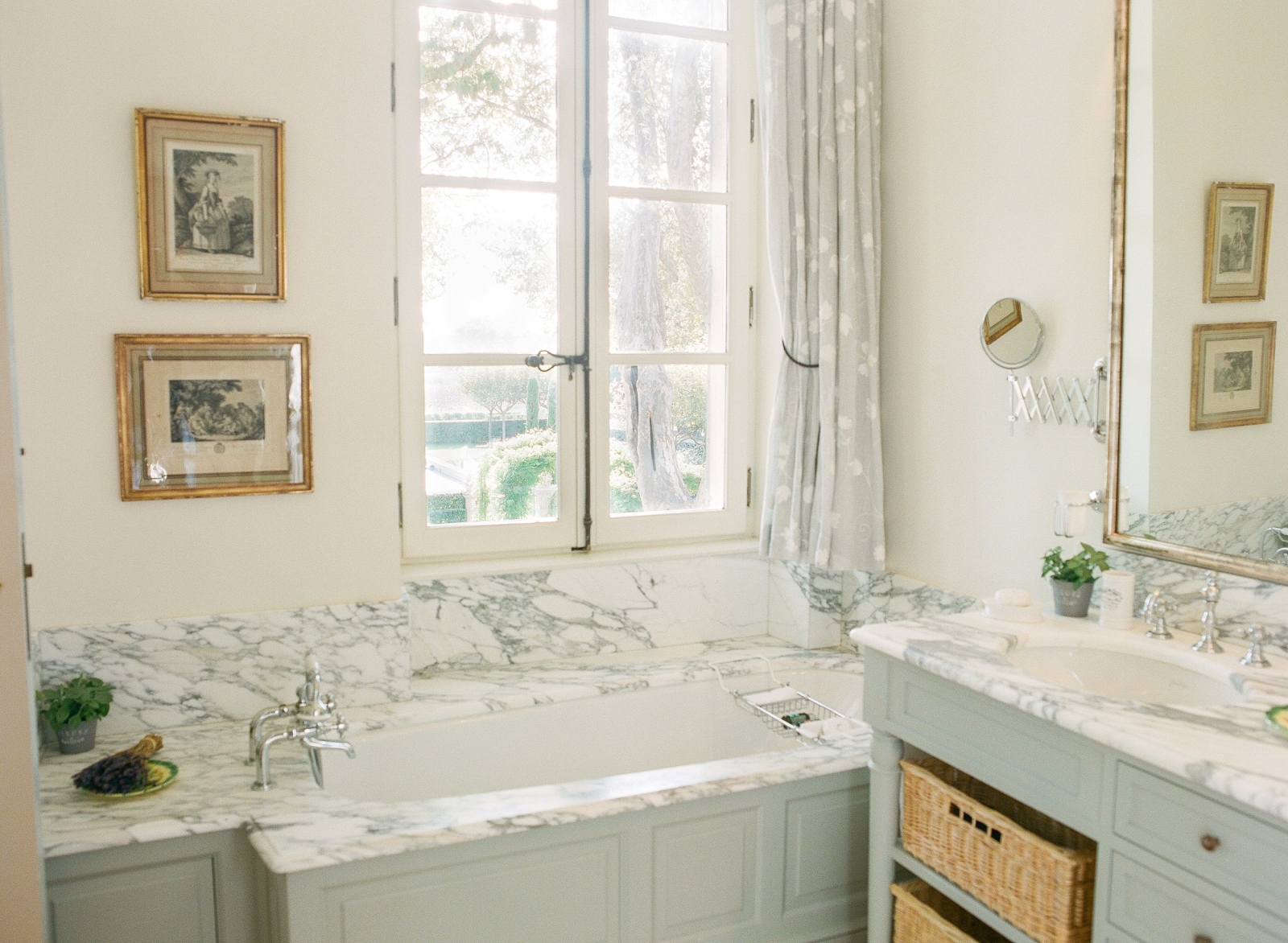 Marble bathroom with bath, sink, large mirror, window and picture frames at Mas de la Motte in Provence, France