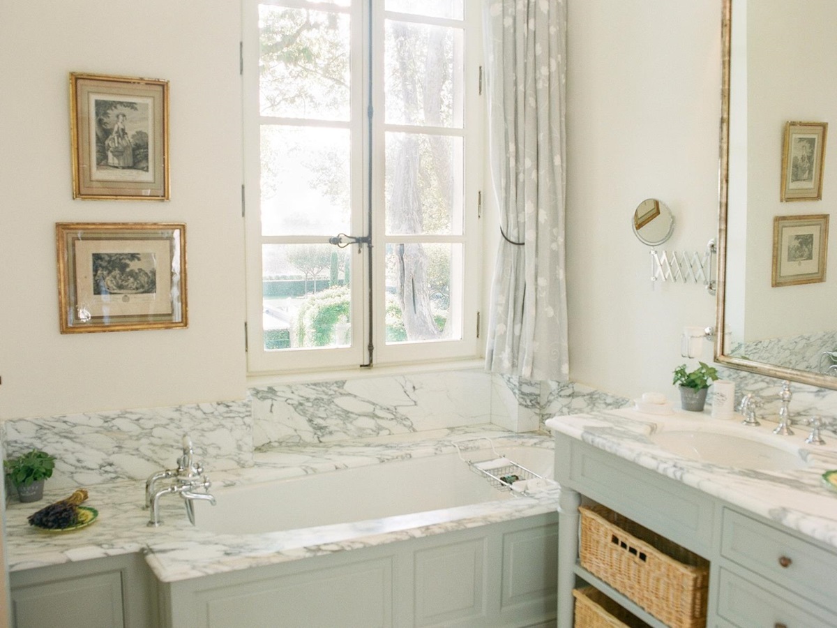 Marble bathroom with bath, sink, large mirror, window and picture frames at Mas de la Motte in Provence, France