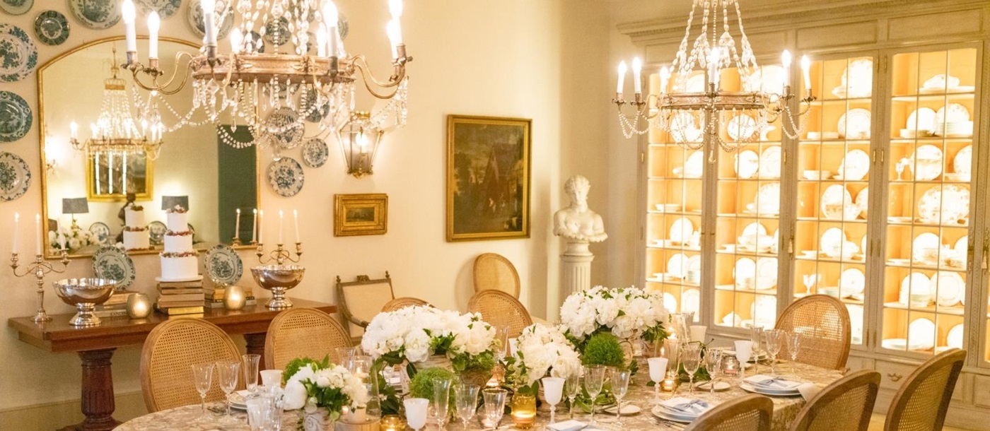 Dining room with chandeliers, candles, flowers, cabinets, mirror and painting at Mas de la Motte in Provence, France