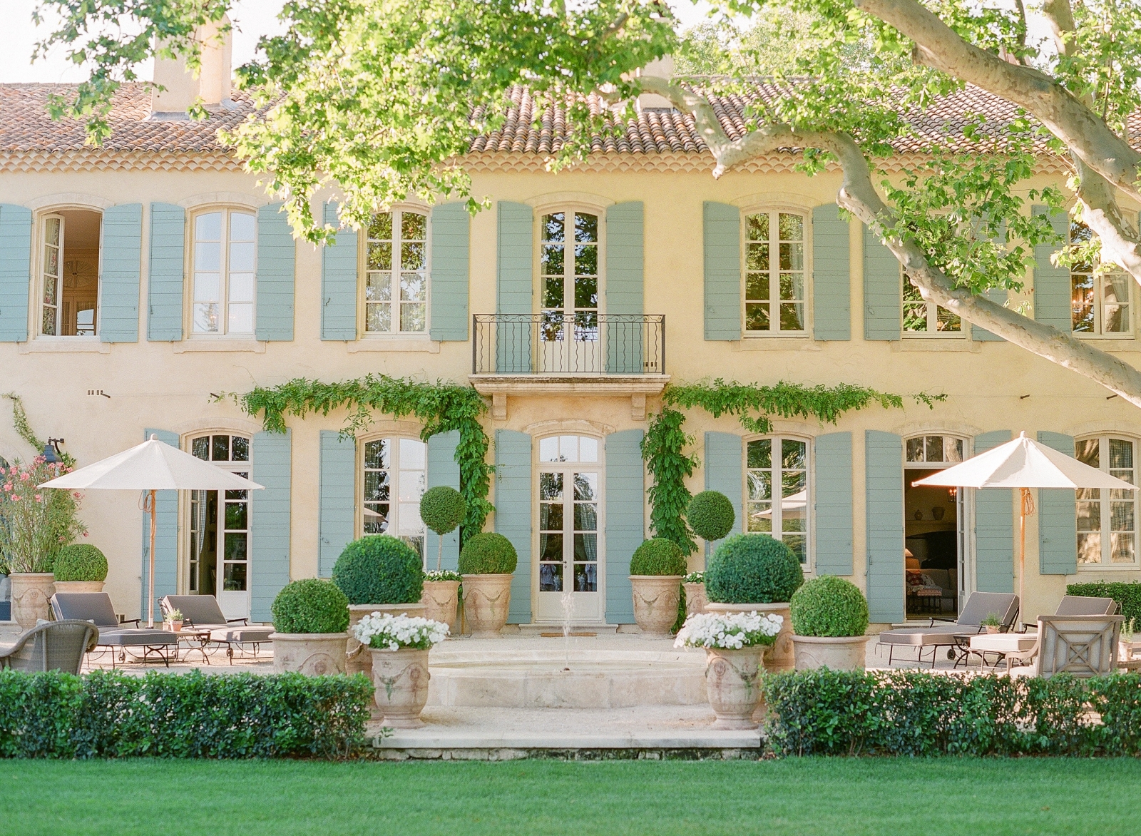 Back of villa and patio with sun loungers, umbrellas, flowers and plants at Mas de la Motte in Provence, France
