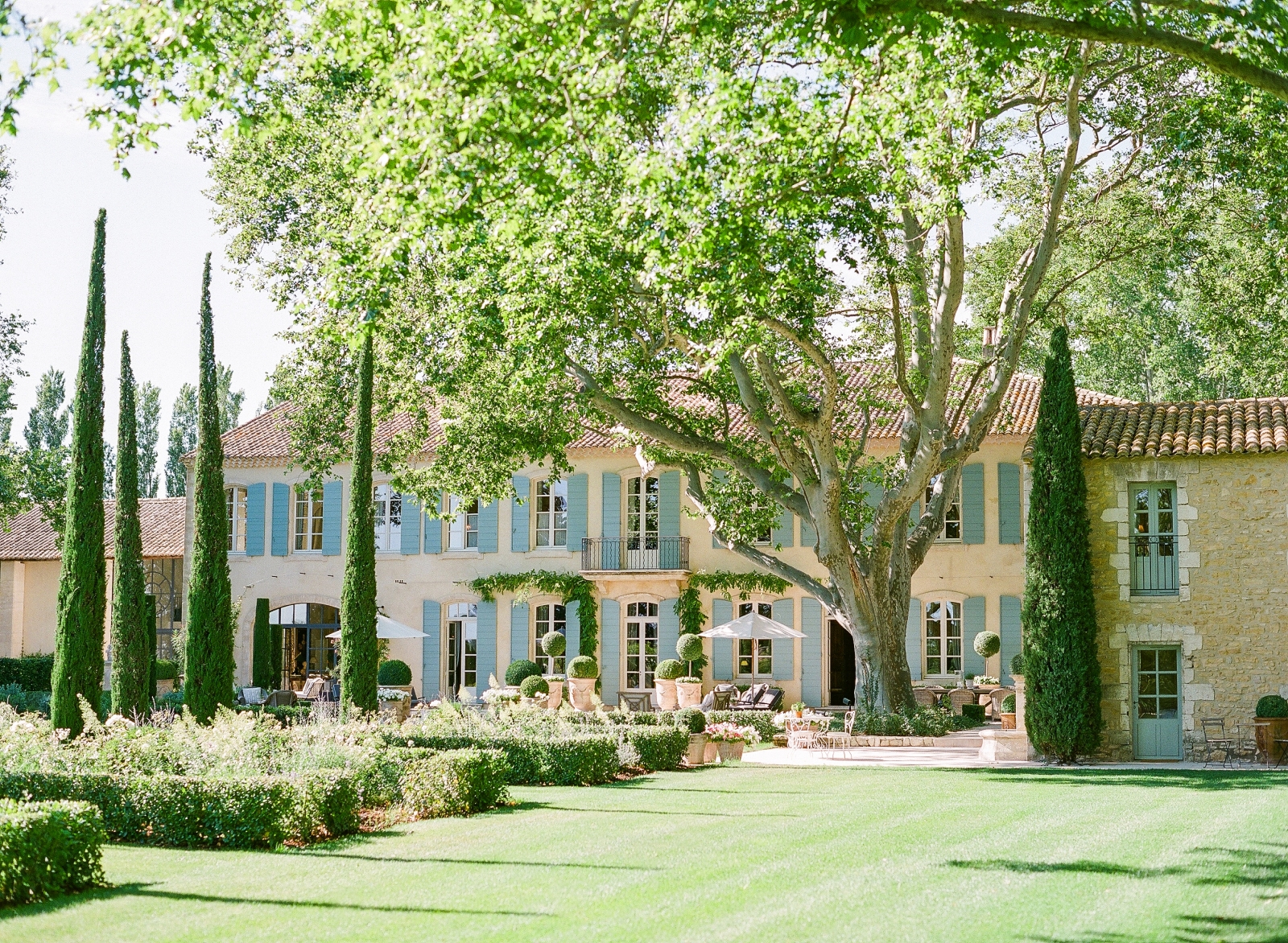 Garden with hedges, lawn, trees next to patio with umbrellas and sunloungers at Mas de la Motte in Provence, France