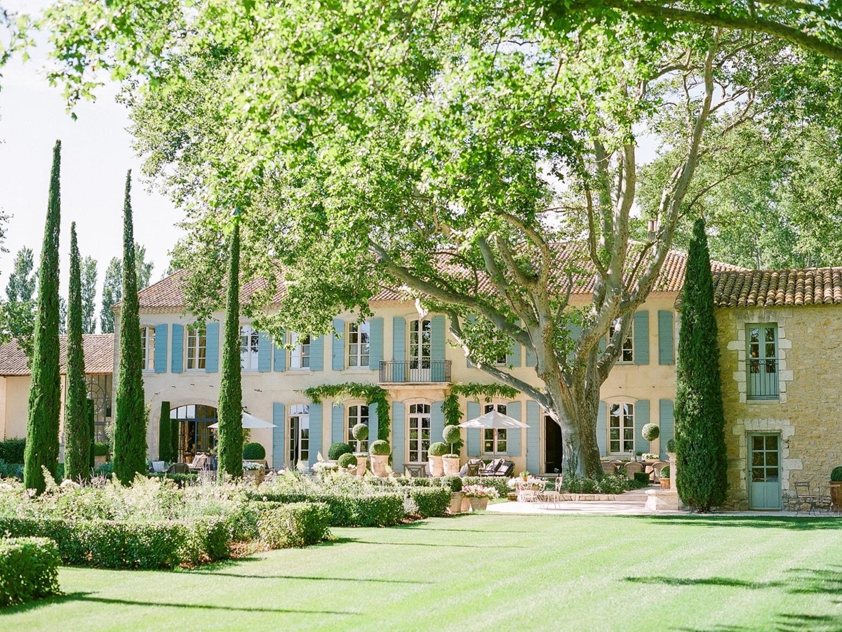 Garden with hedges, lawn, trees next to patio with umbrellas and sunloungers at Mas de la Motte in Provence, France