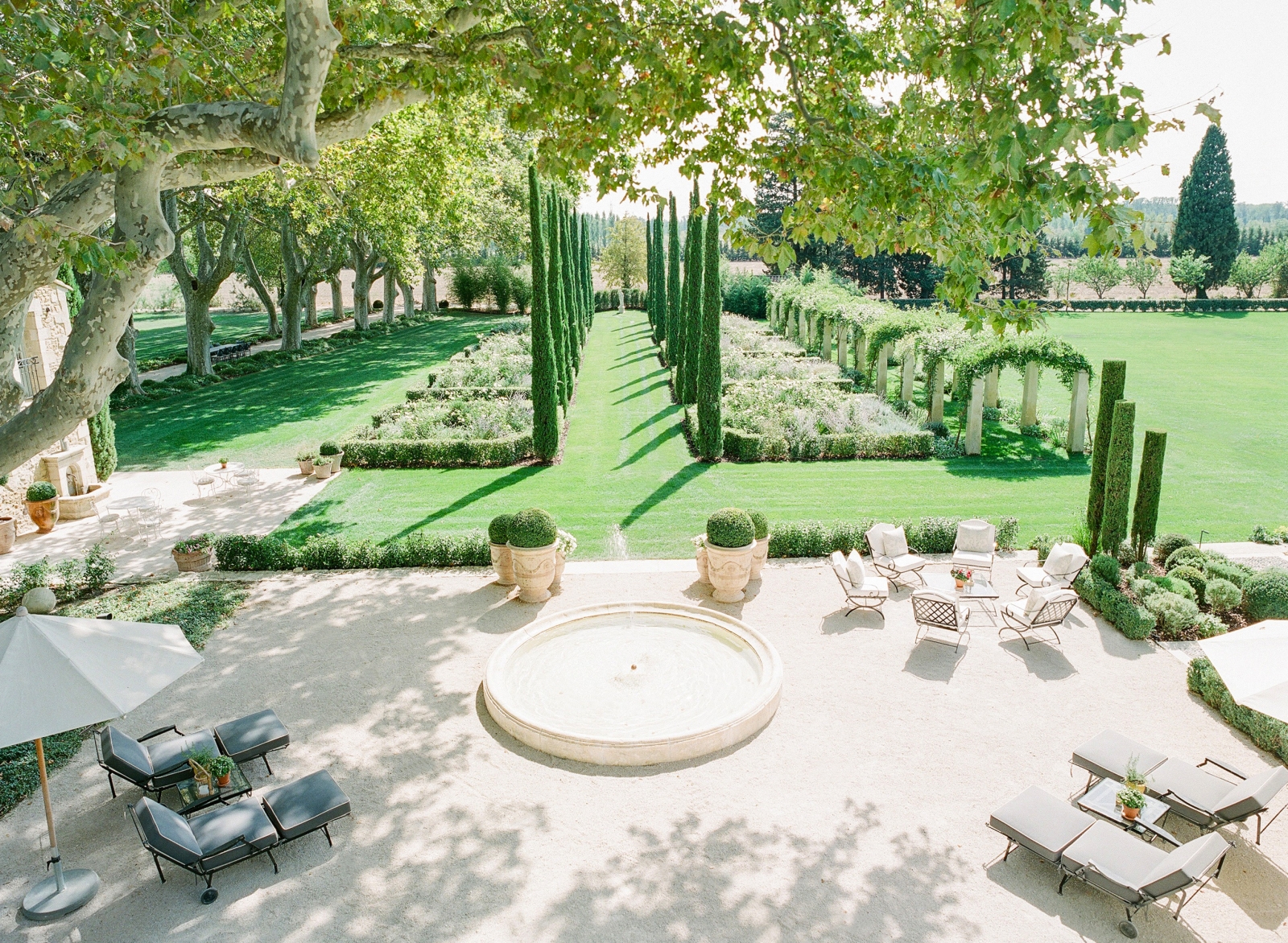 Patio next to garden with sun loungers, fountain, umbrellas, table and chairs at Mas de la Motte in Provence