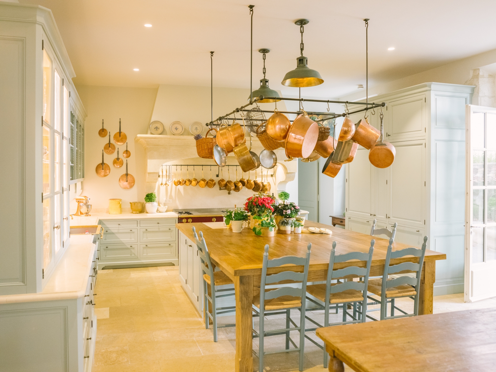 Kitchen with table, chairs, cabinets, hanging saucepans, flowers and appliances at Mas de la Motte in Provence, France