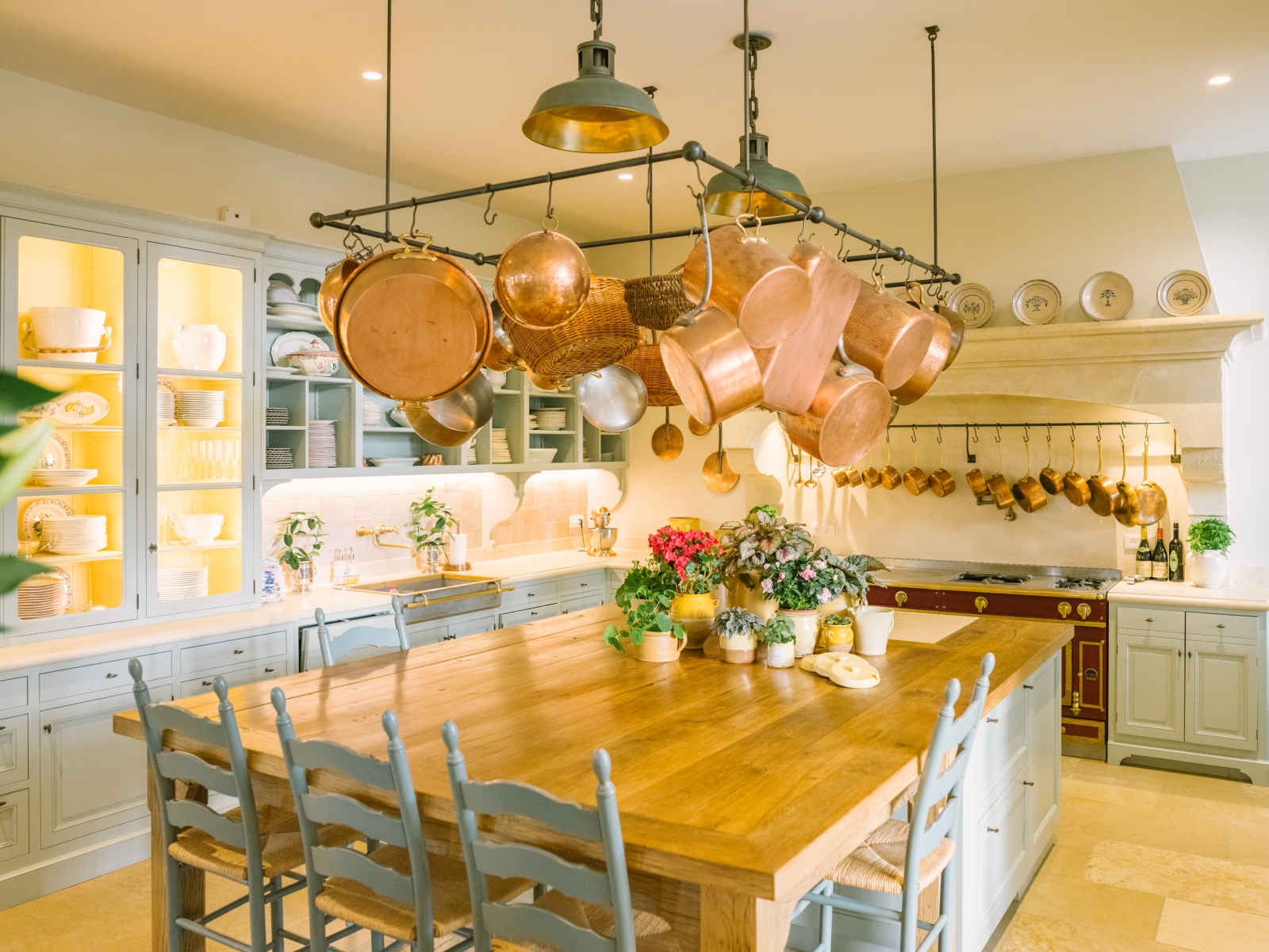 Kitchen with table, chairs, cabinets, hanging saucepans, flowers and appliances at Mas de la Motte in Provence, France