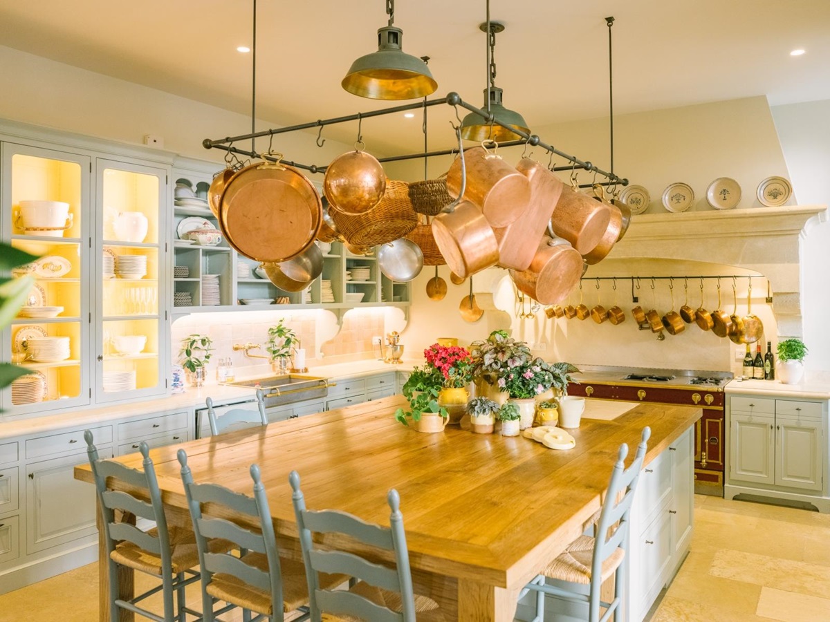 Kitchen with table, chairs, cabinets, hanging saucepans, flowers and appliances at Mas de la Motte in Provence, France