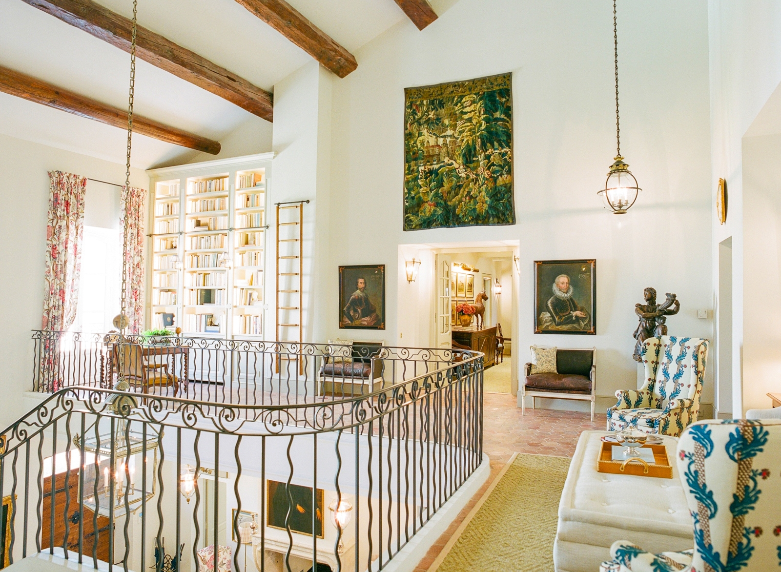 Landing with iron banisters, lights, armchairs, tapestry, bookcase & ceiling beams at Mas de la Motte in Provence, France