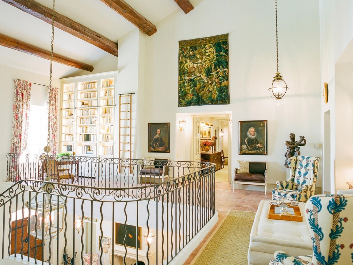 Landing with iron banisters, lights, armchairs, tapestry, bookcase & ceiling beams at Mas de la Motte in Provence, France