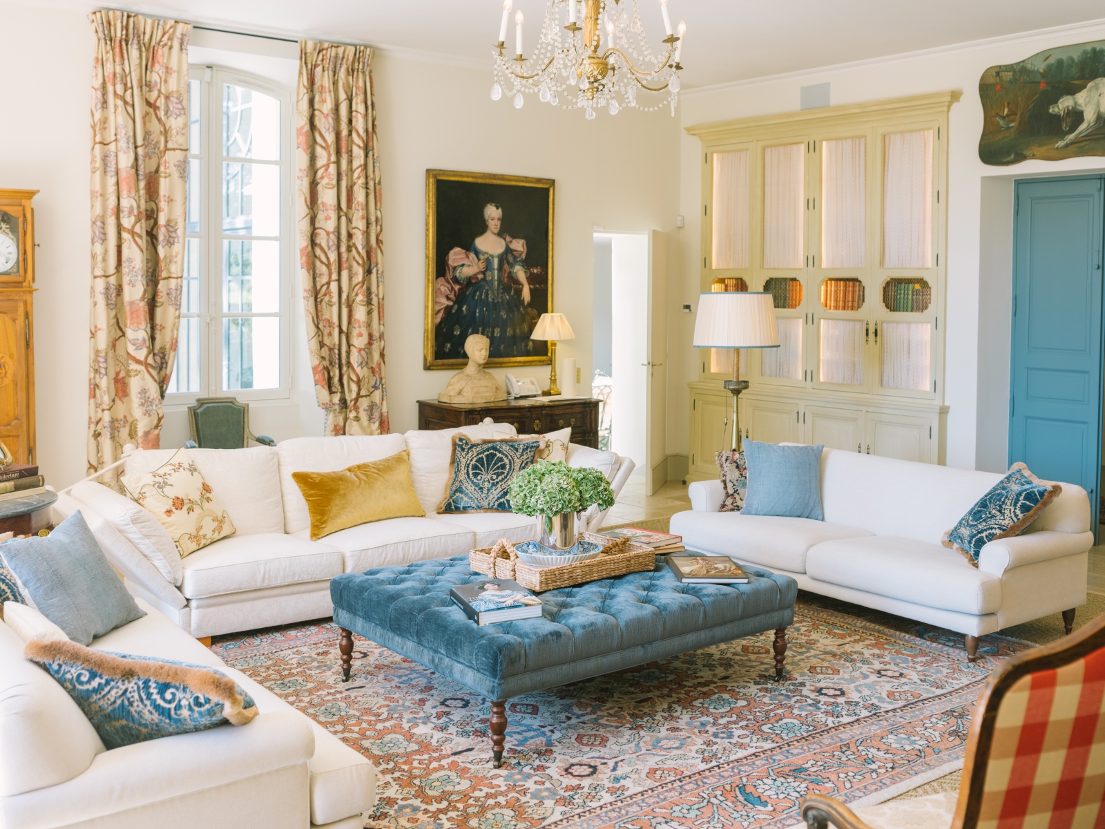Living room with sofas, footstool, chandelier, painting and patterned curtains at Mas de la Motte in Provence, France