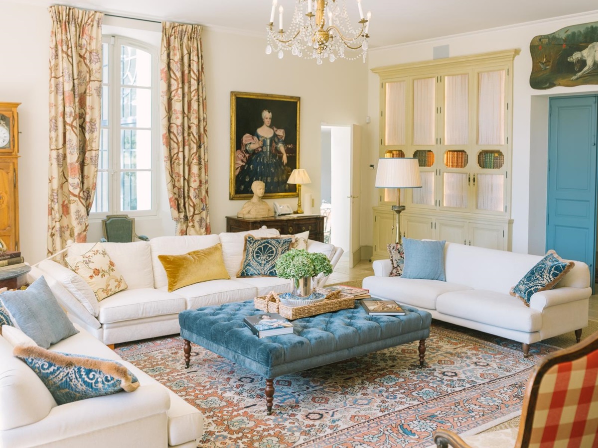 Living room with sofas, footstool, chandelier, painting and patterned curtains at Mas de la Motte in Provence, France